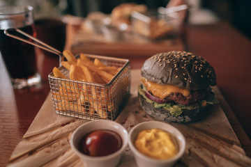 Tasty burger and sauce on wooden tray. Woman eating burger and chips in cafe. People and eating concept. Hamburger, french fries, ketchup, mustard on a wooden board. Toned image.