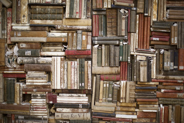 vecchi libri ammucchiati su una parete, accatastati in modo disordinato