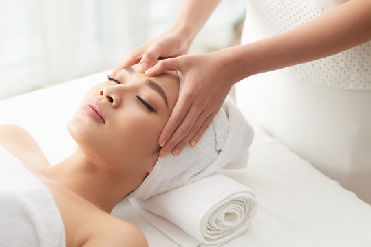 From above shot of unrecognizable woman massaging forehead of beautiful woman while working in spa salon