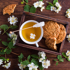 Tea with jasmine and oatmeal cookies on a brown wooden background, white flowers around