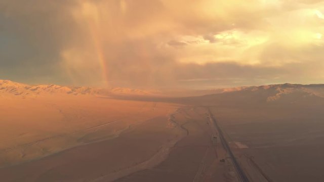 Aerial desert sunset with rainbow, road and colorful sky. Atacama Chile. Drone flying backwards and filming empty road during beautiful evening. Empty vast landscape with warm color grade.