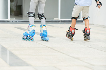 Back view of two children riding roller skates on cement path together