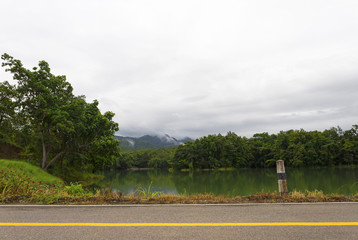 A small lake near the mountains in the rainy morning. Asphalt road along the lake. Perfect for holiday travel.