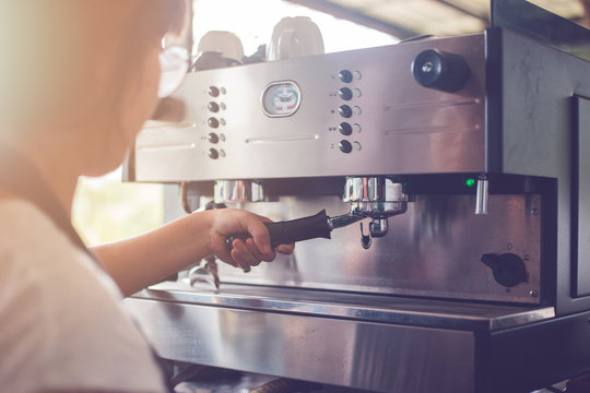 A woman who works in a coffee shop. She was making coffee with coffee machine.