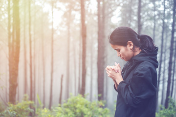 The woman is praying to God in the forest.