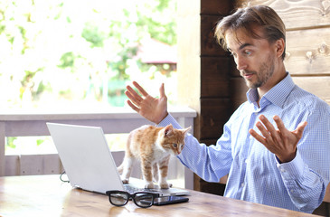 Kitten disturb man working on the laptop. Handsome bearded men work on computer outdoor. Freelance...