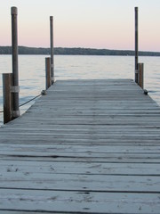 A dock leading out onto a lake with a pink sky at sunset 