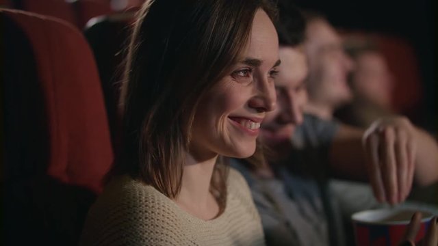 Smiling woman watching movie. Close up of beautiful girl laughing in cinema in slow motion. Boyfriend and girlfriend have fun at movie theater. Romantic date at cinema. Love couple watch comedy film