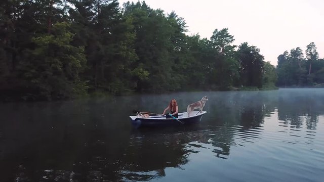 aerial view of young readhead female traveler in the boat on the lake with two siberian husky dogs