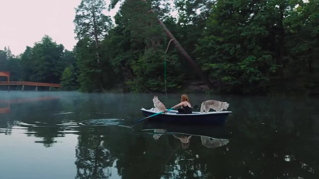 aerial view of young readhead female traveler in the boat on the lake with two siberian husky dogs