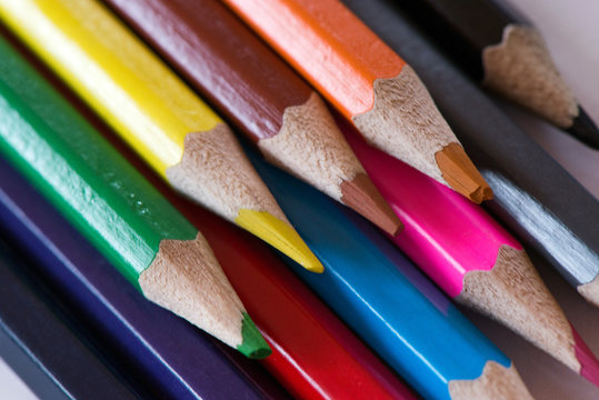 Pile of sharp coloured drawing pencils on table. Rainbow colors  red, yellow, blue, green, purple. Concept of art, crafts and kids having fun
