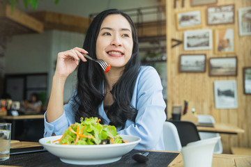 Happy woman eating healthy salad sitting on the table . Beautiful girl eating healthy food. Diet and healthy food concept
