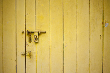 Close-up view of a weathered yellow color door with an open rusty latch