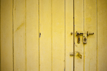 Close-up view of a weathered yellow color door with an open rusty latch