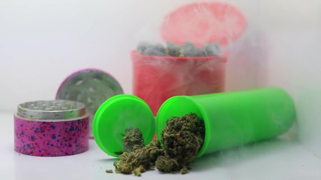 graceful shot of multiple marijuana containers and a grinder being encased and swirled by white smoke