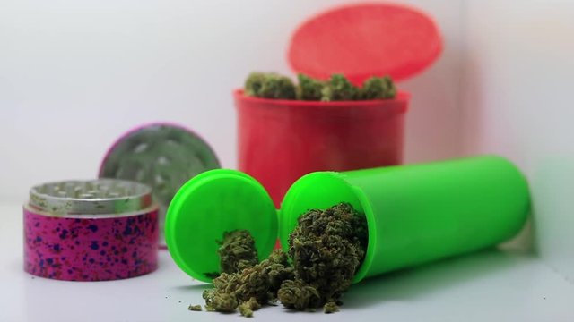 aggresive cloud of white smoke surrounds and engulfs multiple jars of marijuana and grinder in dispensary