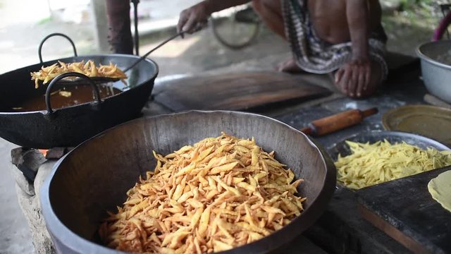 A man picking the frying Indian street snacks Nimki from a Wok with mesh skimmer and putting them in a big utensil