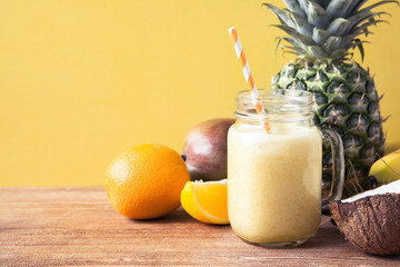 Fresh exotic smoothie with fruits and coconut milk on yellow background.
