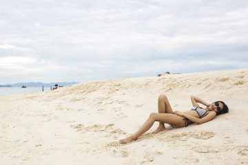 Fototapeta na wymiar Young Asian woman in bikini laying on sandy beach, sexy woman enjoy at the beach