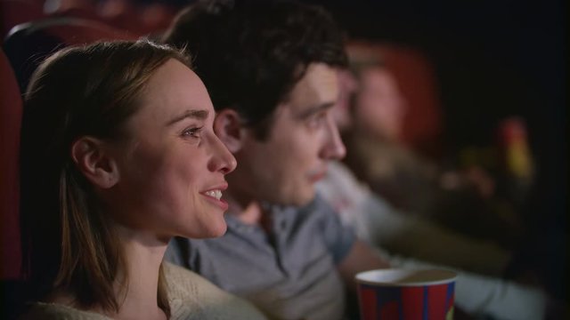 Happy couple watching comedy in cinema. Woman smiling at comedy movie session. Cinema people watching film in slow motion. Joyful people enjoy movie entertainment. Friends enjoy movie