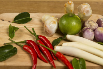 Fresh vegetables on cutting board, chili, lemon grass, lemon leaf set on wooden background. Ingredients for cooking.