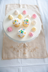 A cake plate contains cupcakes with sprinkles and assorted meringue bites. 