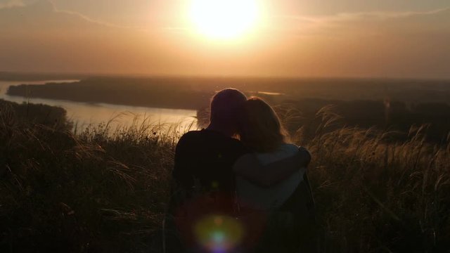 silhouette of a loving couple sitting in a field with a view of the river and sunset