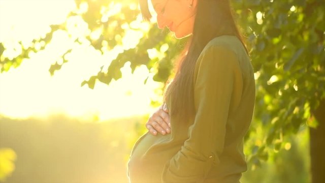 Healthy pregnancy concept. Pregnant woman touching her belly outdoor in summer park. Slow motion. 3840X2160 4K UHD video footage