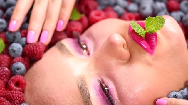 Beauty fashion model girl lying in fresh ripe fruits and berries. Face in colorful berries closeup. Healthy eating concept. Slow motion. 3840X2160 4K UHD video footage