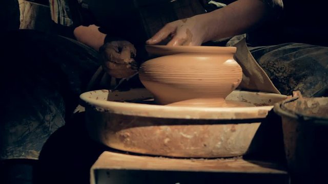 A potter creates patterns on a vase, close up.