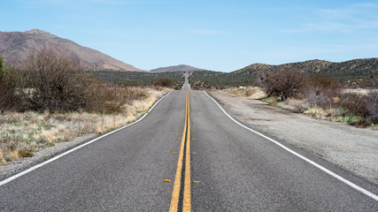 Empty road thru desert landscape. Picture taken in Anza Borrego, CA. Double yellow line on the asphalt makes axis of the picture, hills and blue sky with some white clouds over horizon. Desert flora.