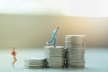 Business, sport and money concept. Two male runner miniature figure running on top of stack of silver coins.