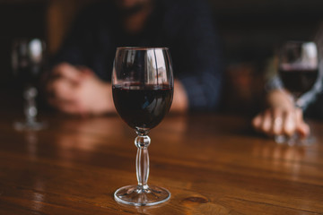 Blurred couple sitting in a restaurant and drink wine. Photos in warm color shades. Focus on glass wine. Glasses of red wine on dinner table close up. Valentine's day, date, love, celebration.
