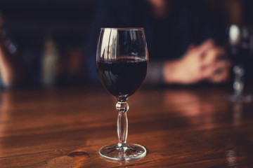 Blurred couple sitting in a restaurant and drink wine. Photos in warm color shades. Focus on glass wine. Glasses of red wine on dinner table close up. Valentine's day, date, love, celebration.