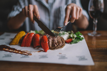 Spicy grilled lamb leg with vegetables and herbs on a roasting cast iron. Barbecue lamb with vegetables. Healthy food. Eating and leisure concept. Woman having dinner at table with food. Toned image.