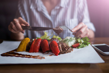 Spicy grilled lamb leg with vegetables and herbs on a roasting cast iron. Barbecue lamb with vegetables. Healthy food. Eating and leisure concept. Woman having dinner at table with food. Toned image.