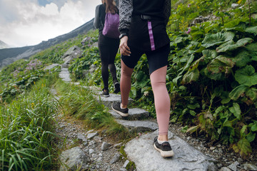 Rear view of women legs close up. Young women in sportswear hiking on the stony pathway in mountains with green hills. © WellStock