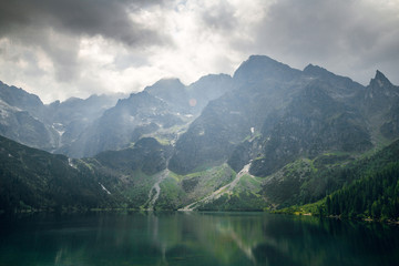 Aerial view shot of beautiful green hills and mountains in dark clouds and reflection on the lake Morskie Oko lake, High Tatras, Zakopane, Poland.