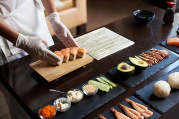 Close-up view of process of preparing rolling sushi. Chef is serving fresh delicious rolls on the wooden board.