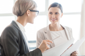 Obraz premium Adult trendy women sitting in bright daylight with papers and having friendly business meeting 