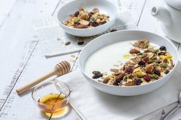 Healthy breakfast: Yogurt with homemade whole grain muesli or granola in a white bowl with honey and coffee on the white table.