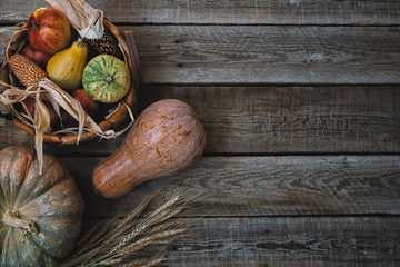 Autumn background with fall leaves, bascet with red apples, corn and pumpkins. Fall harvest on aged wood with copy space. Mockup for seasonal offers and holiday post card, top view. Toned image.