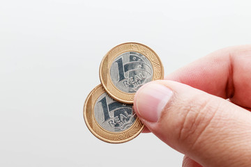Male hand holding two coins of one Real, Brazilian currency white background