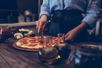 Young woman in kitchen making delicious homemade pizza on rustic kitchen table at home. Italian rural cooking still life. Chef hands preparing homemade food. Healthy foods, cooking concept.