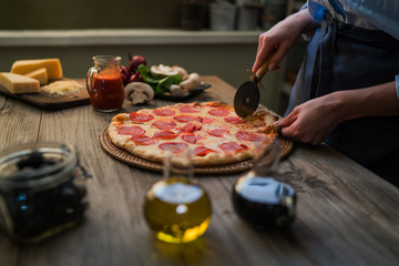 Woman cutting fresh baked homemade pizza on rustic kitchen background. Cut into slices delicious...