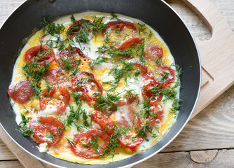 Scrambled eggs with tomatoes and dill in a frying pan