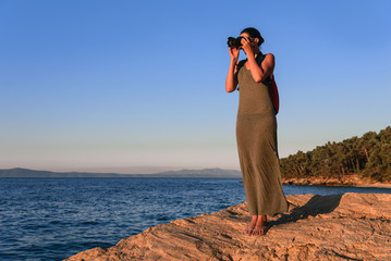 Woman with a camera photographing the sunset on the sea coast.