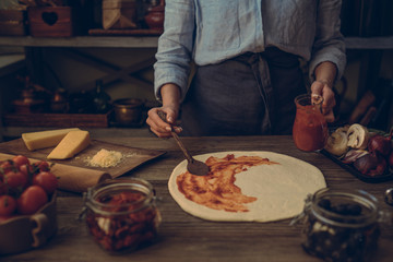The process of making pizza. Prepare dough hand topping. Woman hand is spreading pasteurized tomato paste onto a pizza base. Food concept. Preparing traditional italian pizza. Toned image.