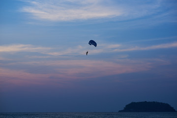 Sunset over the ocean. Silhouette of a lonely parachute on sunset background. Sky, clouds and water. Beautiful serene scene. Natural composition of nature. Landscape. Concept of outdoor activities..