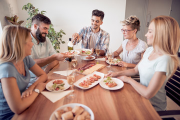 Obraz na płótnie Canvas Smiling friends having dinner and drinking wine at home